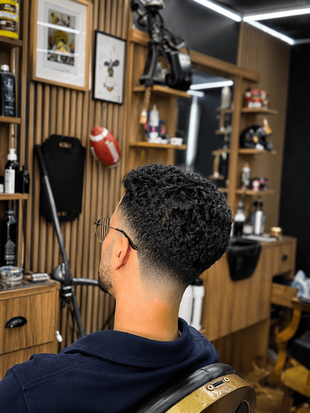 Hombre con cabello rizado oscuro y un corte degradado preciso en una barbería de madera.